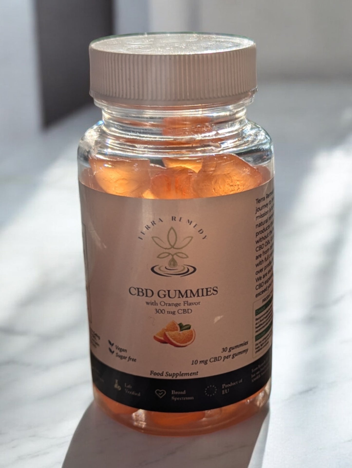 
                  
                    A bottle of Terra Remedy Orange Flavor CBD Gummies, containing 300mg CBD with 30 gummies, displayed on a reflective surface.
                  
                
