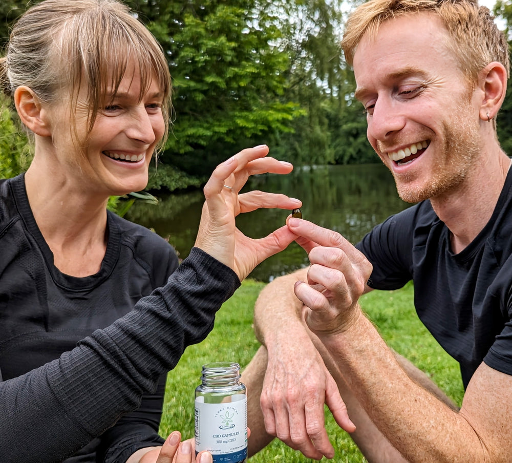 A couple smiling while holding a single CBD capsule between their fingers, with a bottle of Terra Remedy CBD capsules in the foreground. The image highlights the convenience and ease of use of the 300 mg CBD capsules for daily wellness.