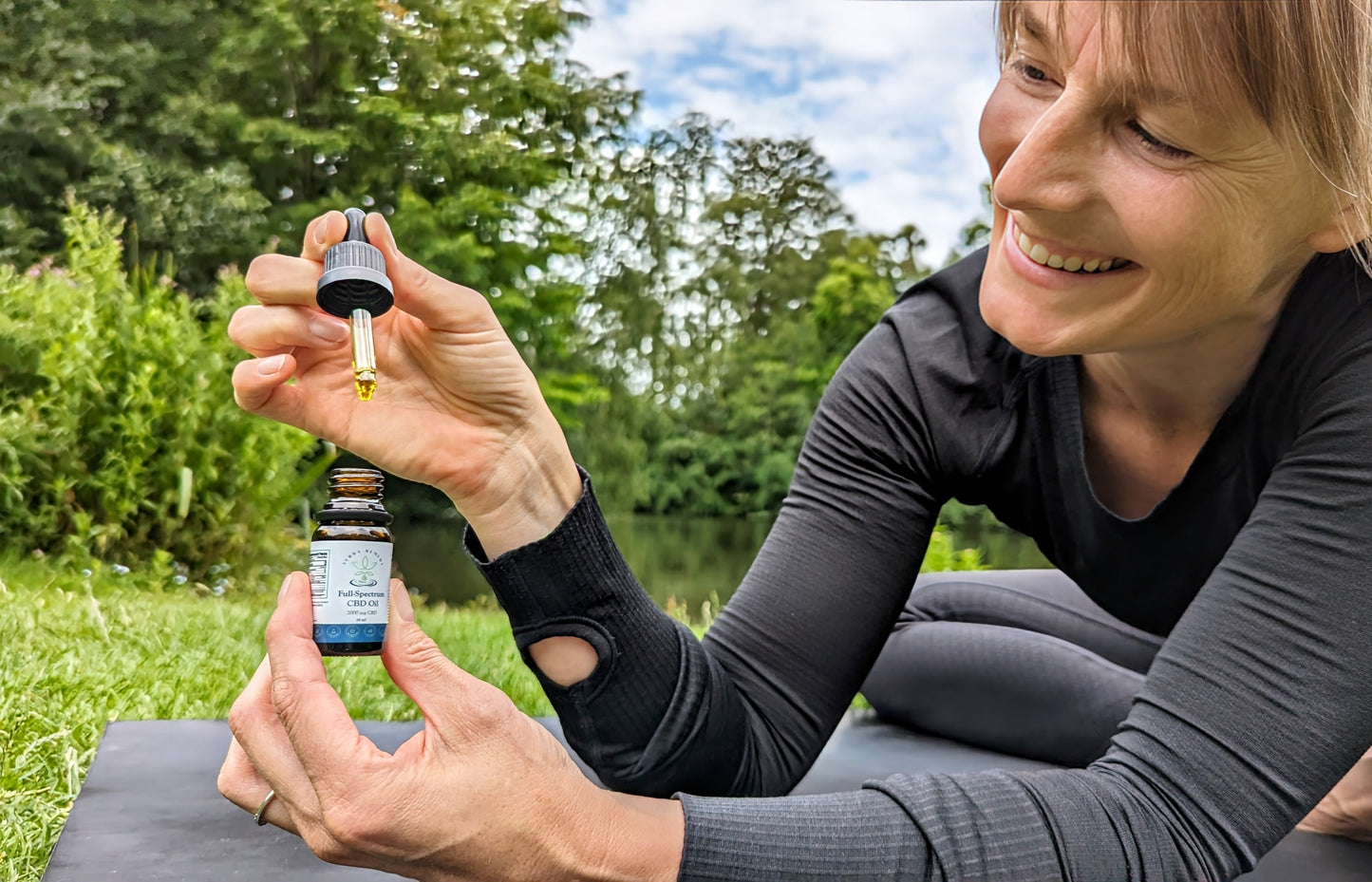 
                  
                    A person smiling while holding a dropper of Terra Remedy Full-Spectrum CBD Oil. The dropper showcases the rich, golden color of the oil, emphasizing its natural, lab-tested formula for versatile wellness support.
                  
                