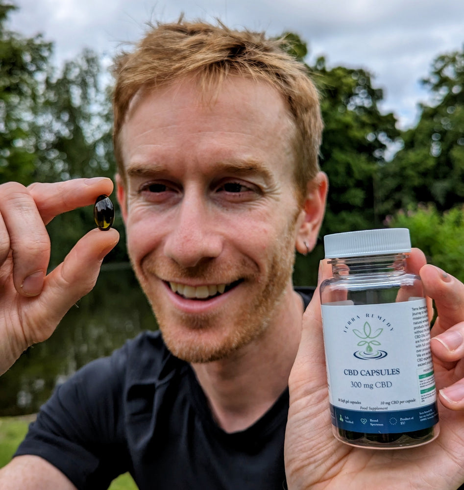 
                  
                    A person smiling while holding a single CBD capsule and a bottle of Terra Remedy CBD capsules containing 300 mg of broad-spectrum CBD. The image highlights the size and convenience of the soft gel capsules for daily use.
                  
                